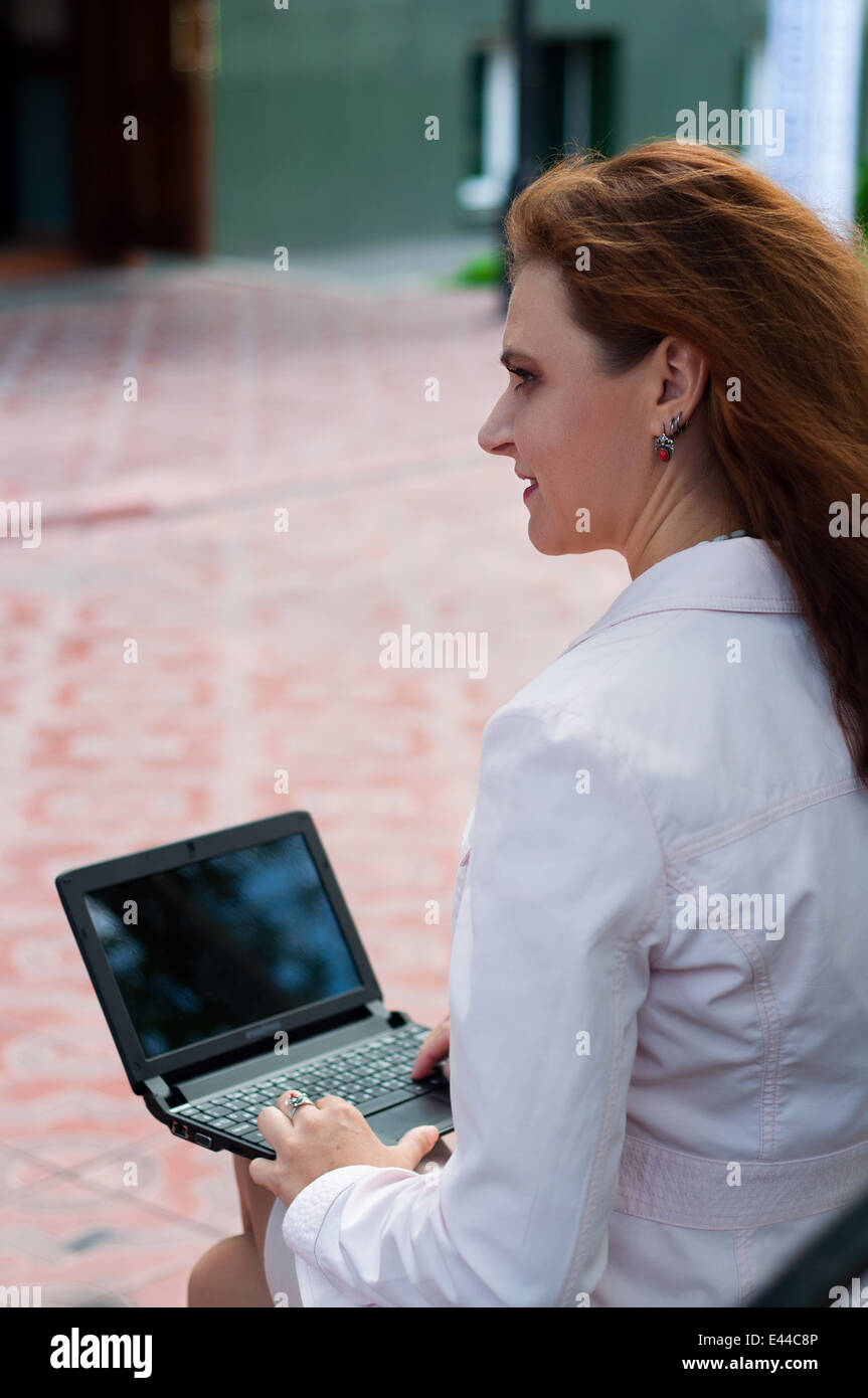 Young caucasian woman holding laptop sitting in downtown Stock Photo