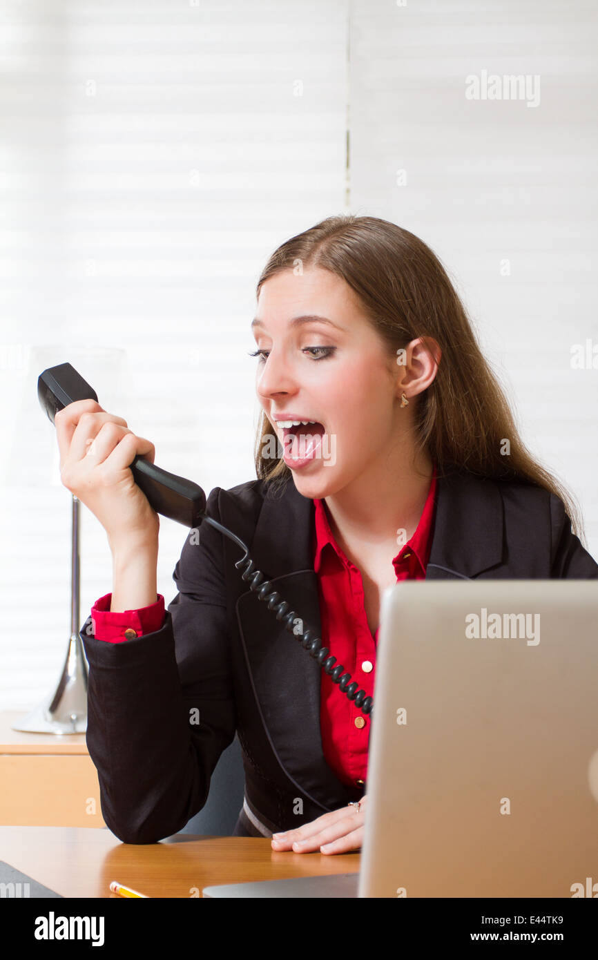 A  young executive woman shouts to the phone at the office Stock Photo