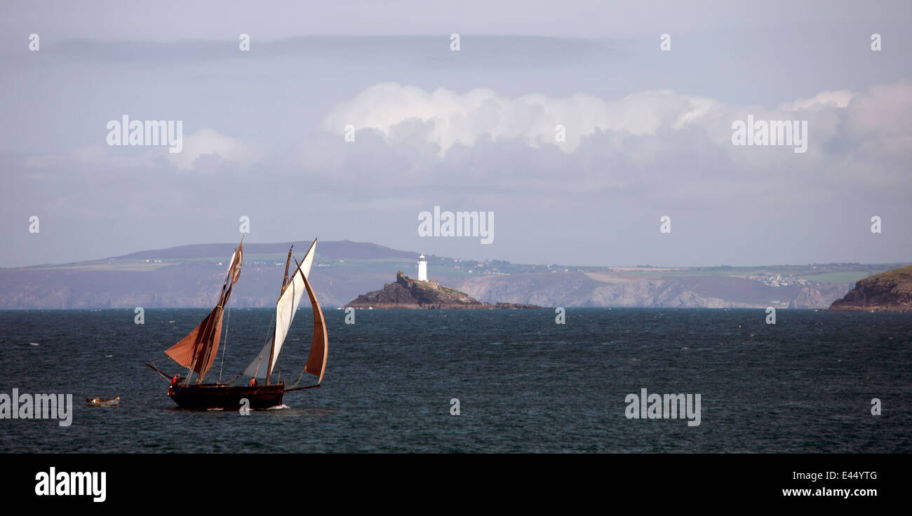 An ancient lugger, Cornish fishing boat, sailing across St. Ives Bay, Cornwall, UK, with Godrevy Lighthouse in the background. Stock Photo