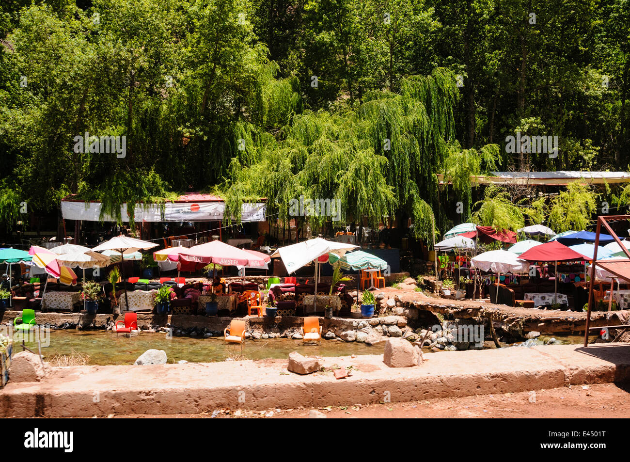 Plastic patio tables, chairs with parasols at restaurants on the banks of the Ourika River, Ourika Valley, Atlas Mountains, Morocco Stock Photo