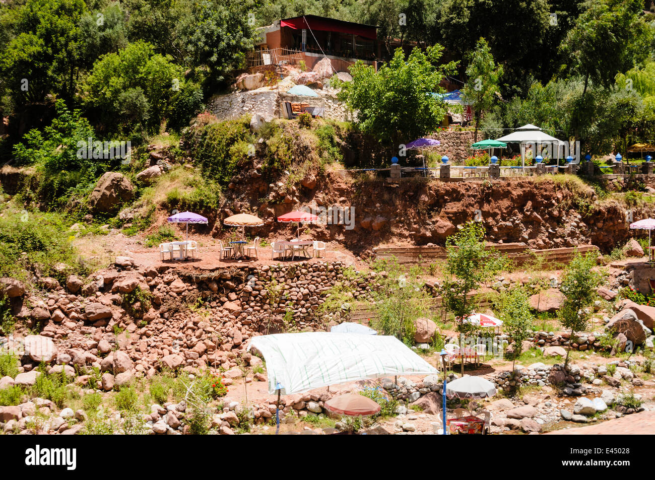 Plastic patio tables, chairs with parasols at restaurants on the banks of the Ourika River, Ourika Valley, Atlas Mountains, Morocco Stock Photo