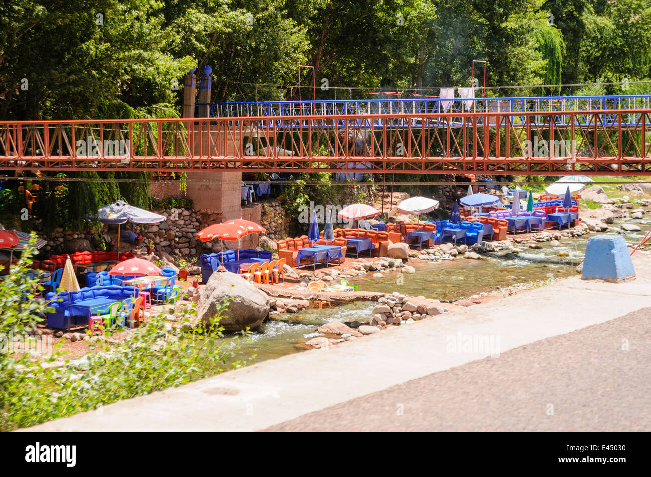 Plastic patio tables, chairs with parasols at restaurants on the banks of the Ourika River, Ourika Valley, Atlas Mountains, Morocco Stock Photo