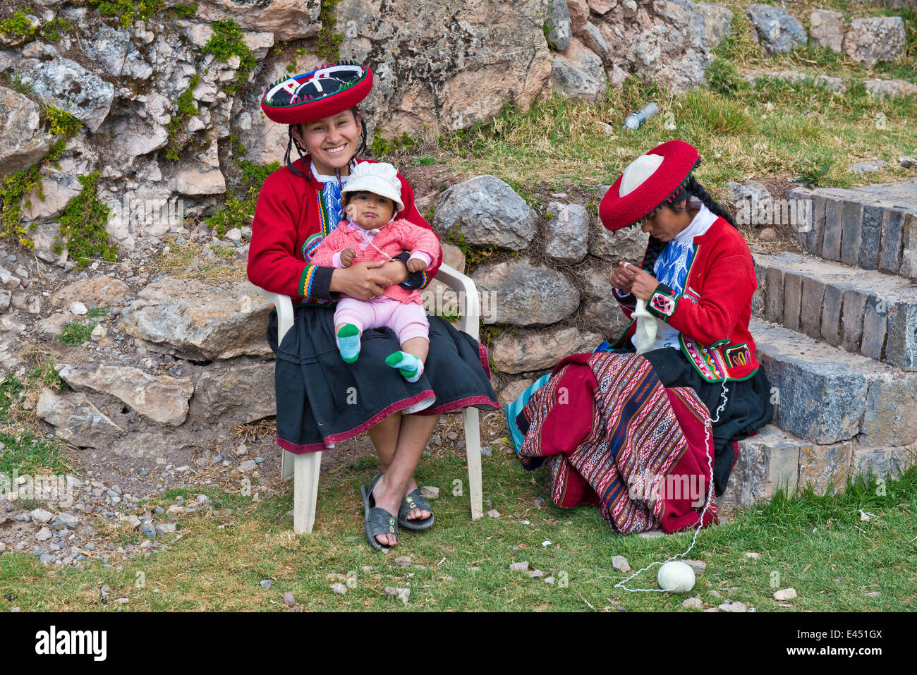 Two women, Quechua Indians, in traditional dress, one smiling woman sitting on a chair holding a toddler, another woman sitting Stock Photo