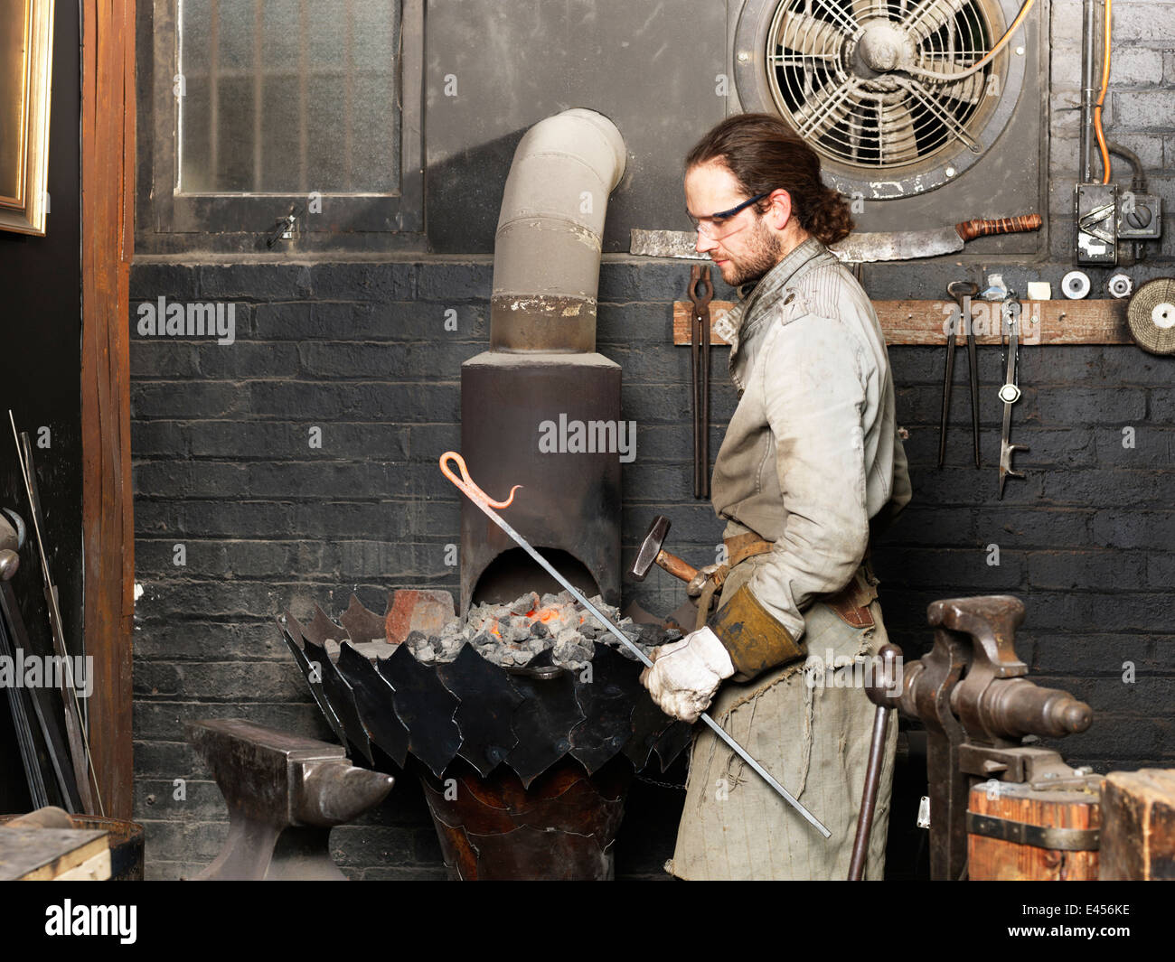 Blacksmith with a red hot metal rod in workshop Stock Photo