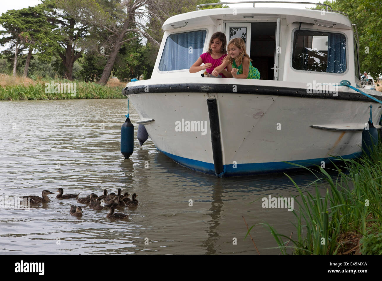 Girls feeding mallard ducks from a boat cruising on the Canal Du Midi near Capestang, Languedoc, France. July 2009. Model and property released. Stock Photo