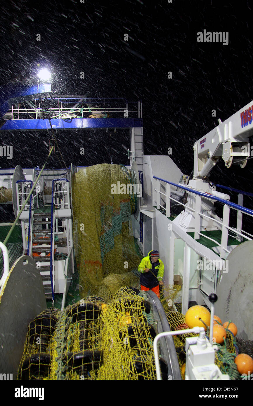 Trawlerman mending nets on fishing vessel's trawl deck during a wintry night on the North Sea, February 2010. Model and property released. Stock Photo