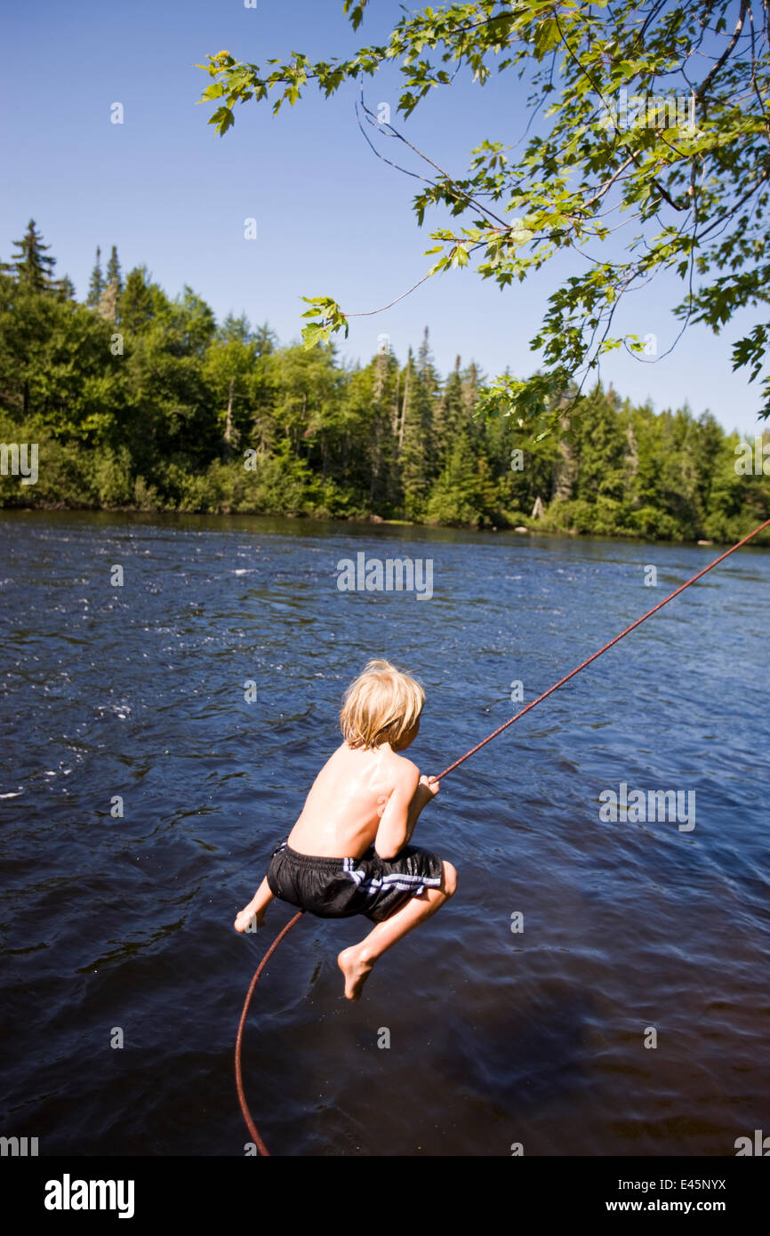 Boy playing on rope swing over the Androscoggin River, Mollidgewock State Park in Errol, New Hampshire, USA, August 2008. Model released. Stock Photo