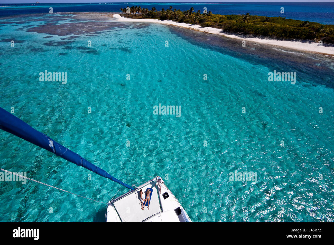 Couple sunbathing on the trampoline of a catamaran in the Grenadines, viewed from the masthead. Caribbean. February 2010. Stock Photo