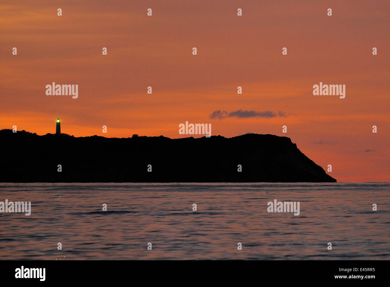Lighthouse flashing on Hiddensee island, silhouetted on Baltic sea horizon at sunset, viewed from Rugen island, Mecklenberg-Vorpommern, Germany. Stock Photo