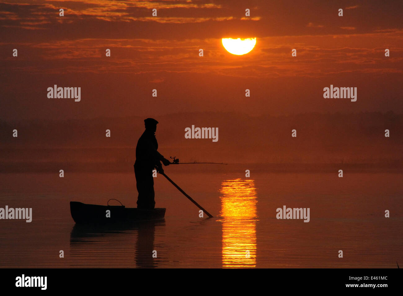 Fisherman silhouetted angling from traditional punt as the sun rises over the Biebrza river and marshes, Biebrza National Park, Podlaskie, Poland, May 2008. Stock Photo