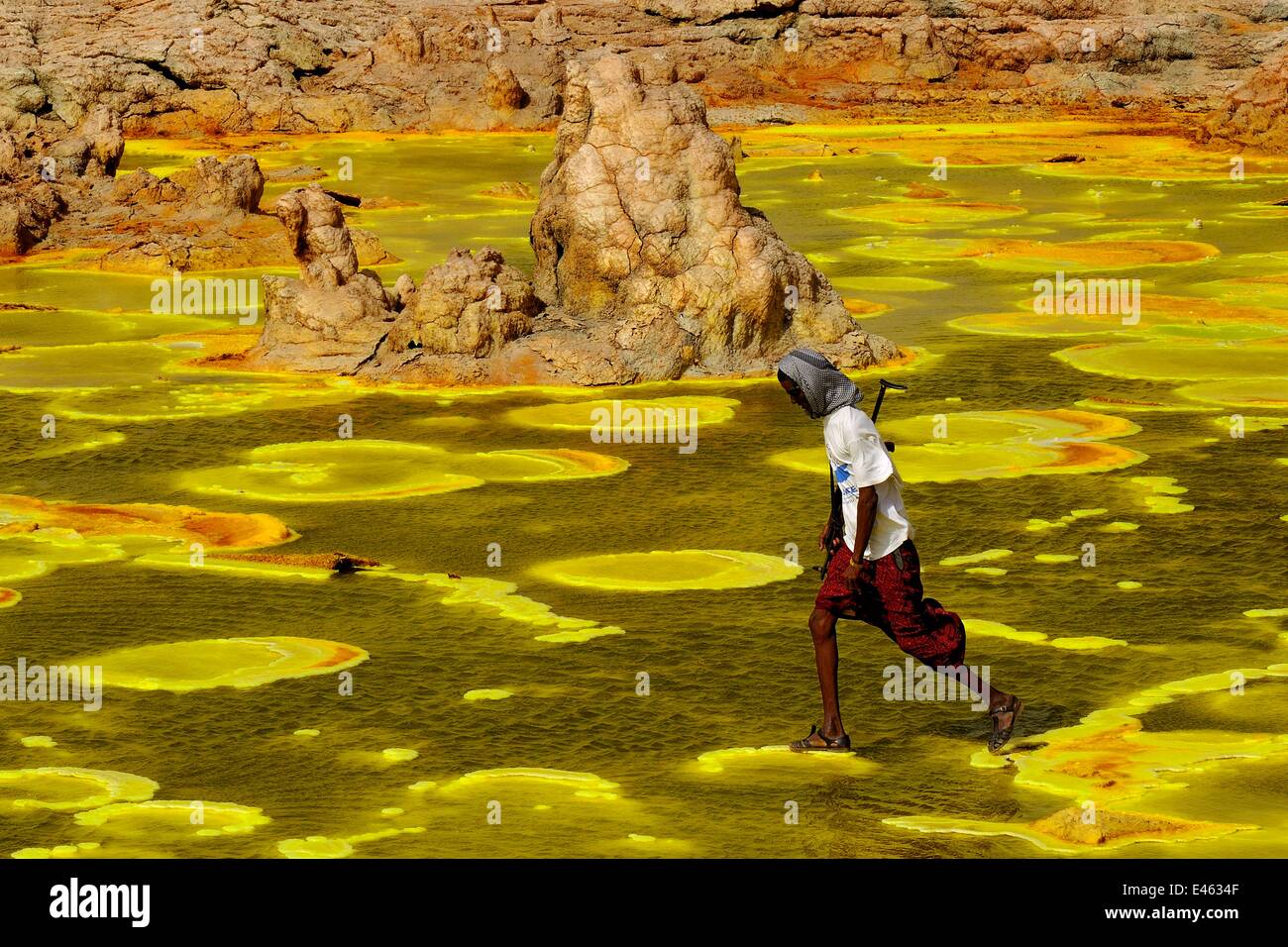 Man walking over colourful mineral deposits at the Dallol hydrothermal site on the Karoum salt lake, Danakil depression,  northern Ethiopia, February 2009 Stock Photo