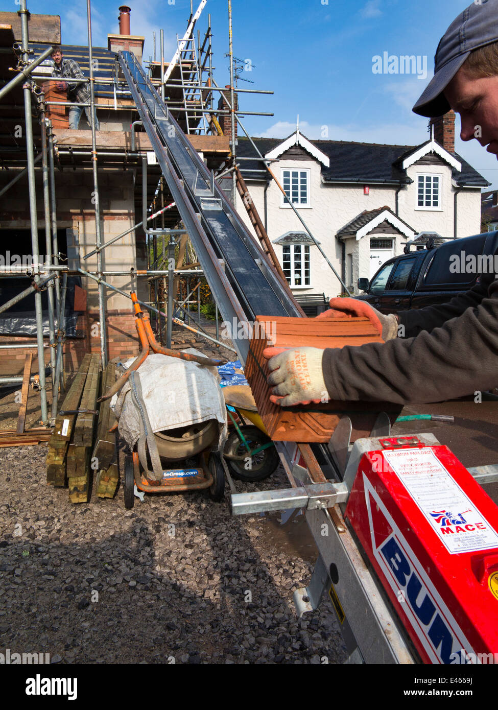 self building house, man using Bumpa lift to elevate clay roofing tiles to scaffolding Stock Photo