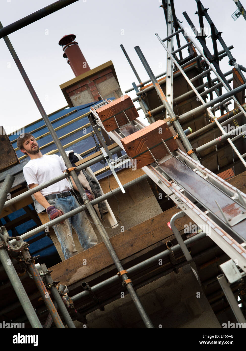 self building house, man using Bumpa lift to elevate clay roofing tiles to scaffolding Stock Photo