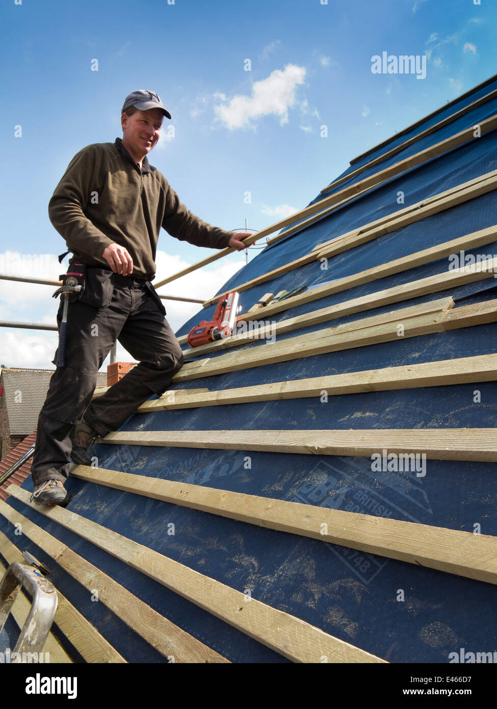 self building house, constructing roof, man nailing roofing laths with