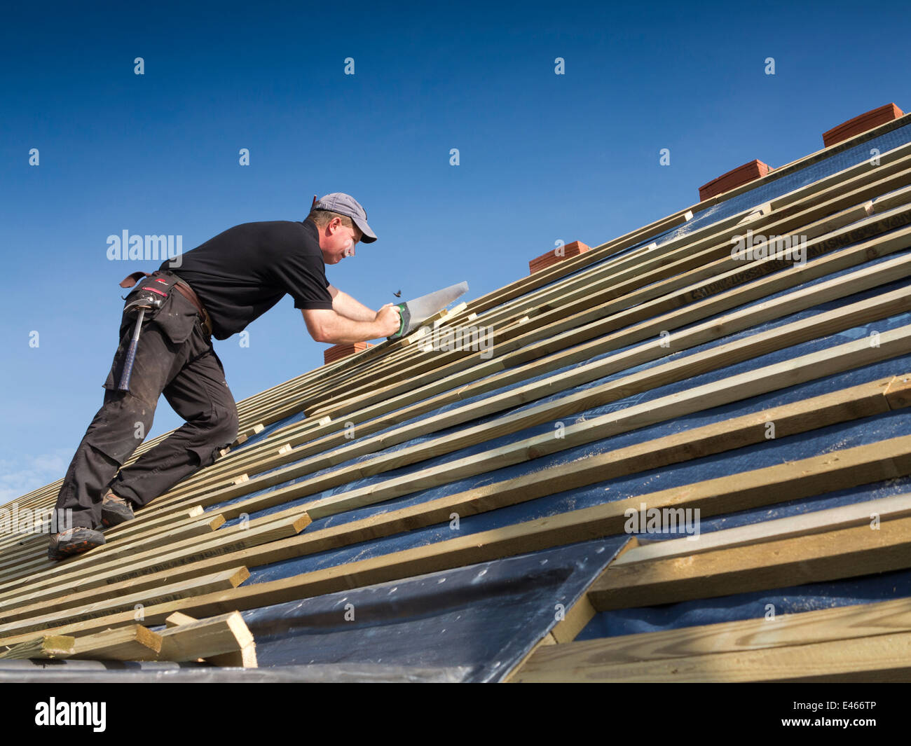 self building house, constructing roof, man sawing roofing laths with