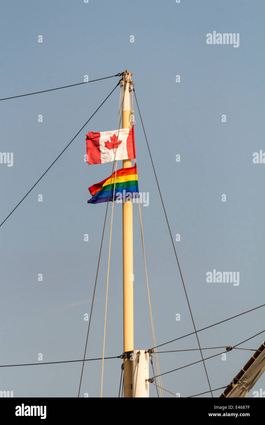 Canadian flag and the Pride Rainbow Flag atop a mast on a tall ship in Toronto Harbour during World Pride Week. Stock Photo