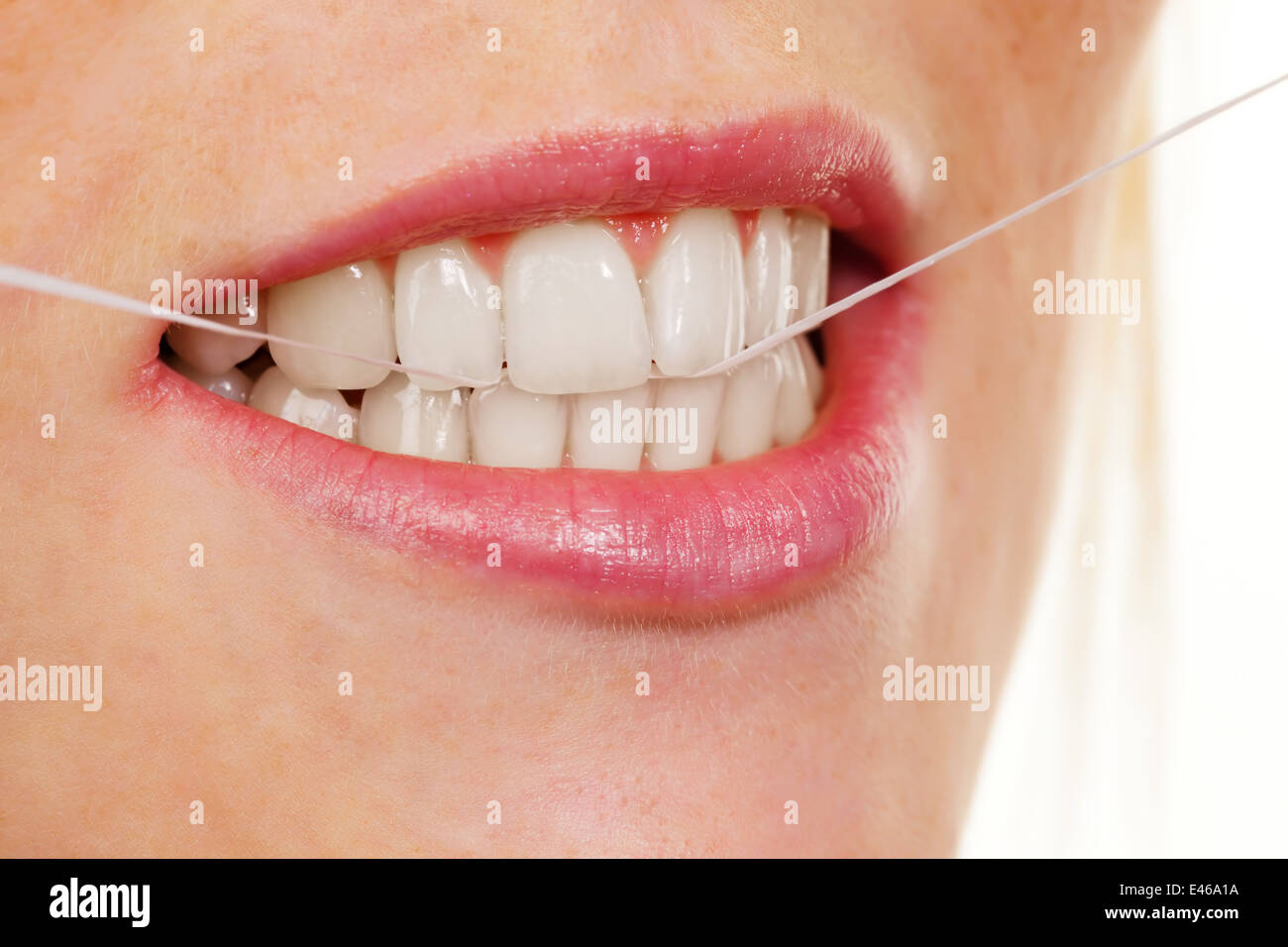 A young woman uses dental floss to clean her teeth Stock Photo