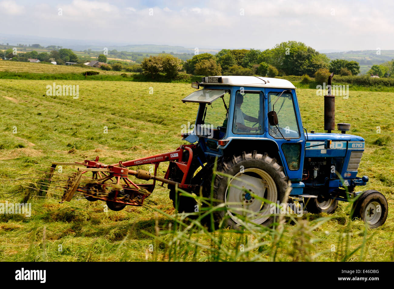Farm tractor with "hay bob" rake turning grass to aid drying for hay or