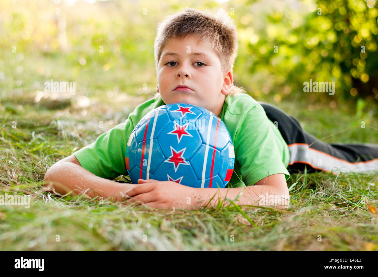 boy child alone ball soccer football eight years nature park square summer day sunny sports t-shirt grass sport blond sitting ma Stock Photo