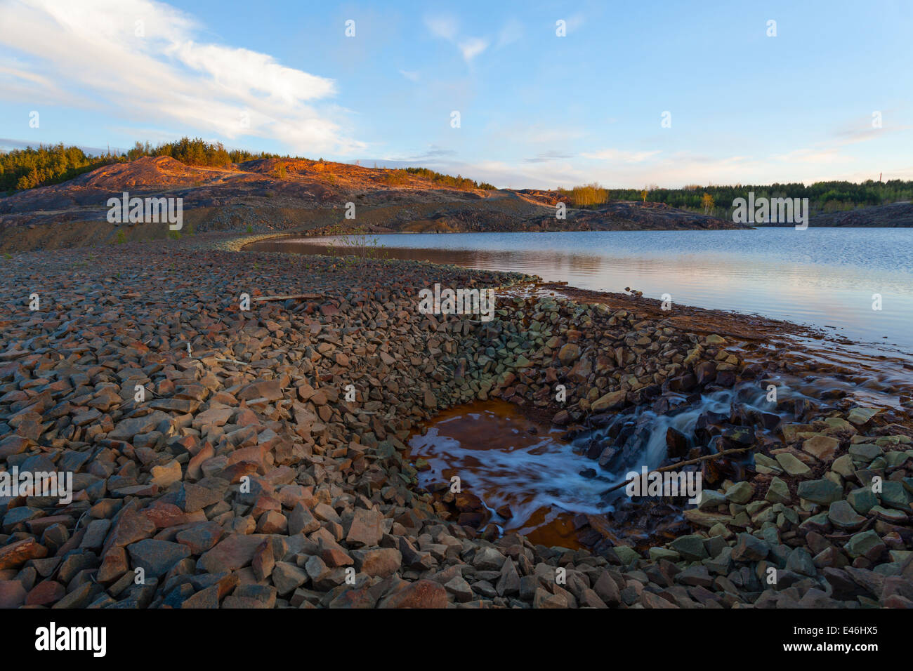 Strong rusty, red and brown colours cover the rocky dam that contains the tailings pond in Sudbury near the Vale Mine. Stock Photo