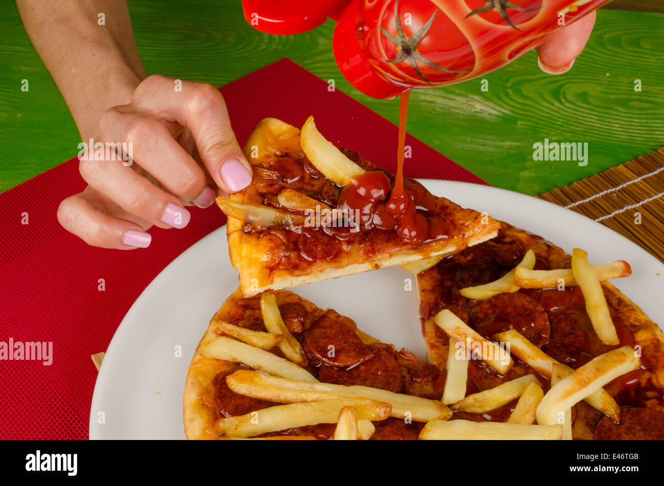 Pouring ketchup on pizza garnished with French fries, a junk food