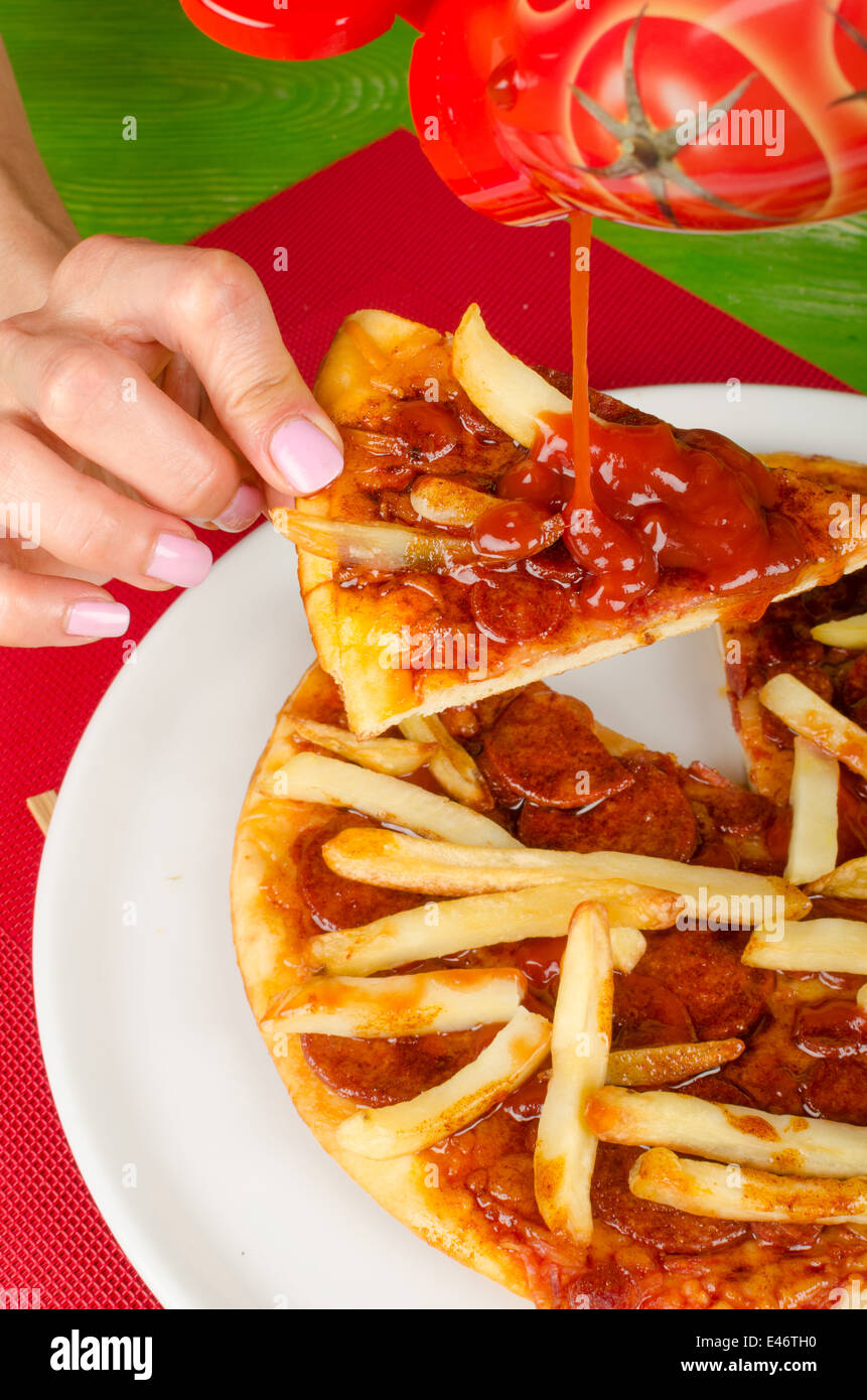 Pouring ketchup on pizza garnished with French fries, a junk food