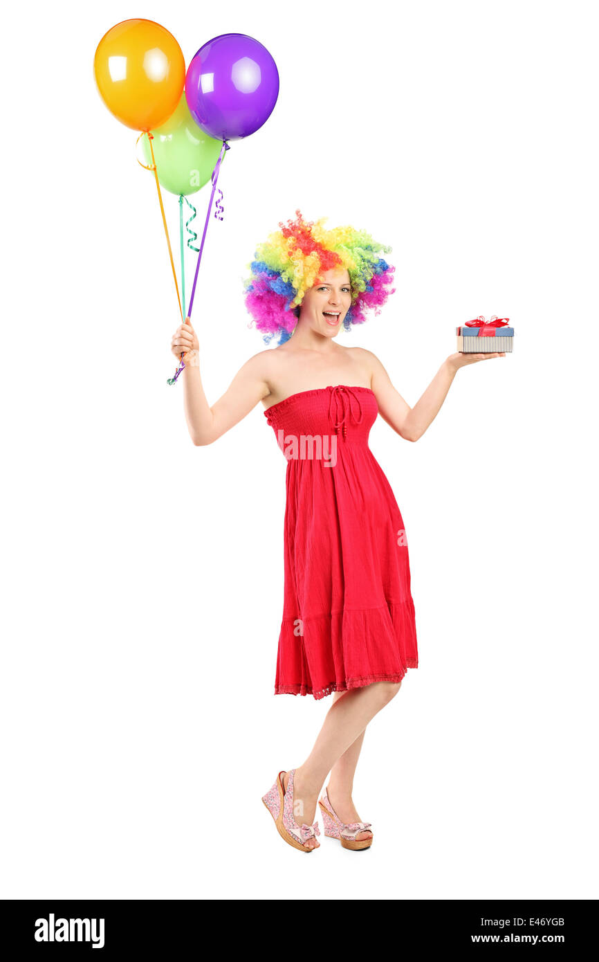 Full length portrait of a woman wearing a wig and holding a present and a bunch of balloons Stock Photo