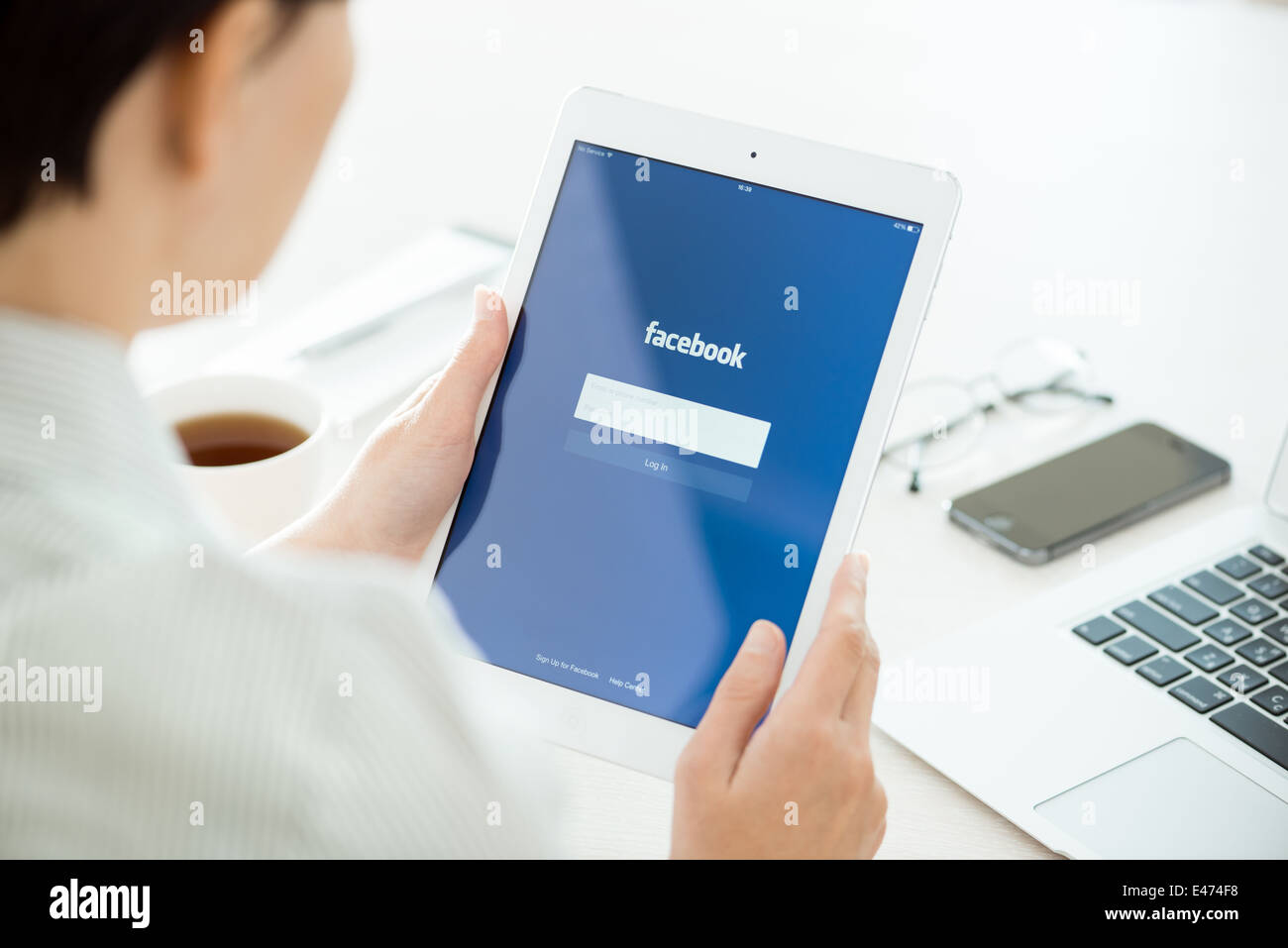 Woman looking on Facebook application login page on modern white Apple iPad Air, which is designed and developed by Apple inc Stock Photo