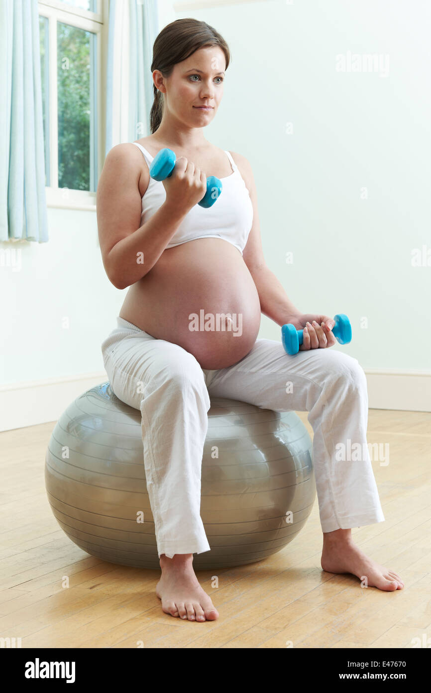 Pregnant Woman Sitting On Exercise Ball With Weights Stock Photo