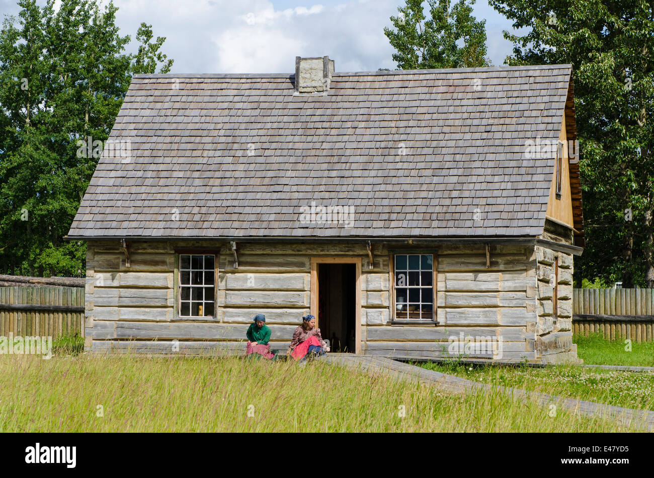 People sitting old log cabin house building Fort Saint St James