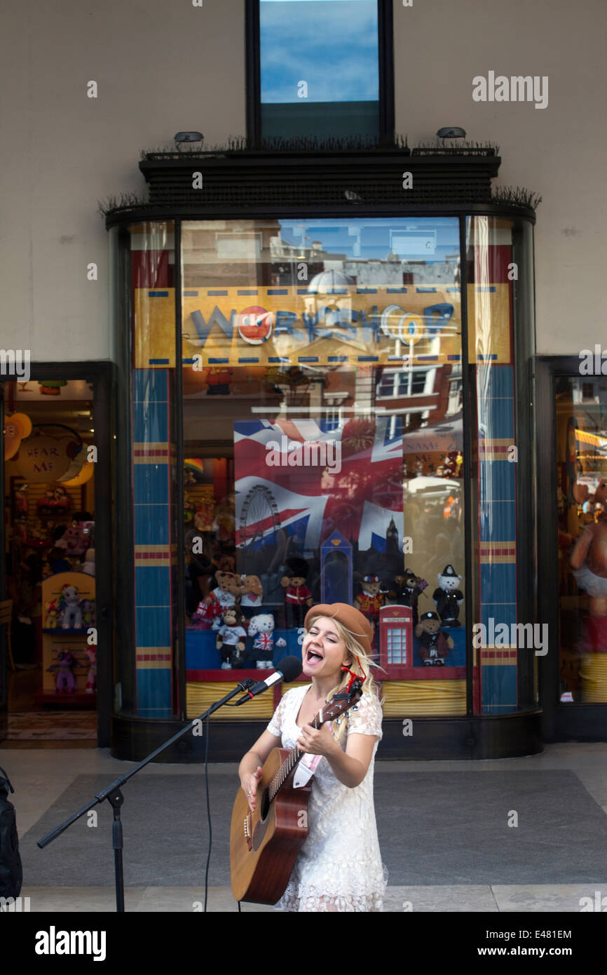 A female busker sings and plays guitar to a crowd in Covent Garden Market, London, UK Stock Photo