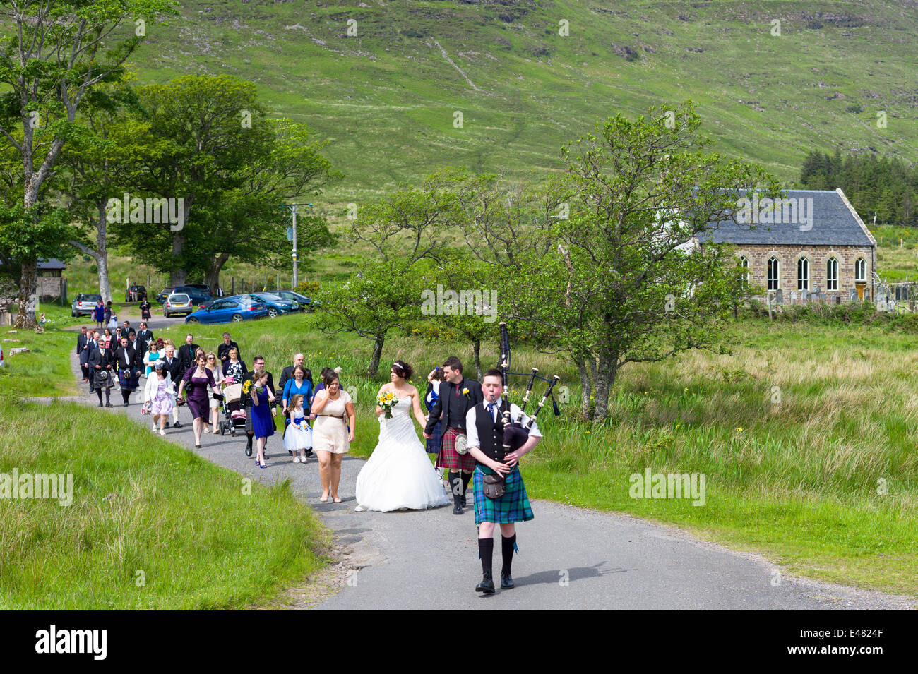 Highland Scottish wedding.  Piper leads procession of bride, groom and guests from Clachan Church in the Highlands of SCOTLAND Stock Photo
