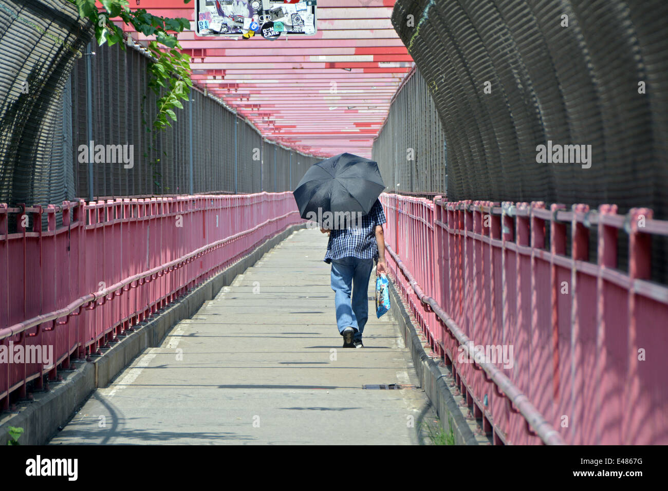 A man walking on the bicycle and walkers path on the Williamsburg Bridge in Brooklyn, New York on a hot summer day Stock Photo