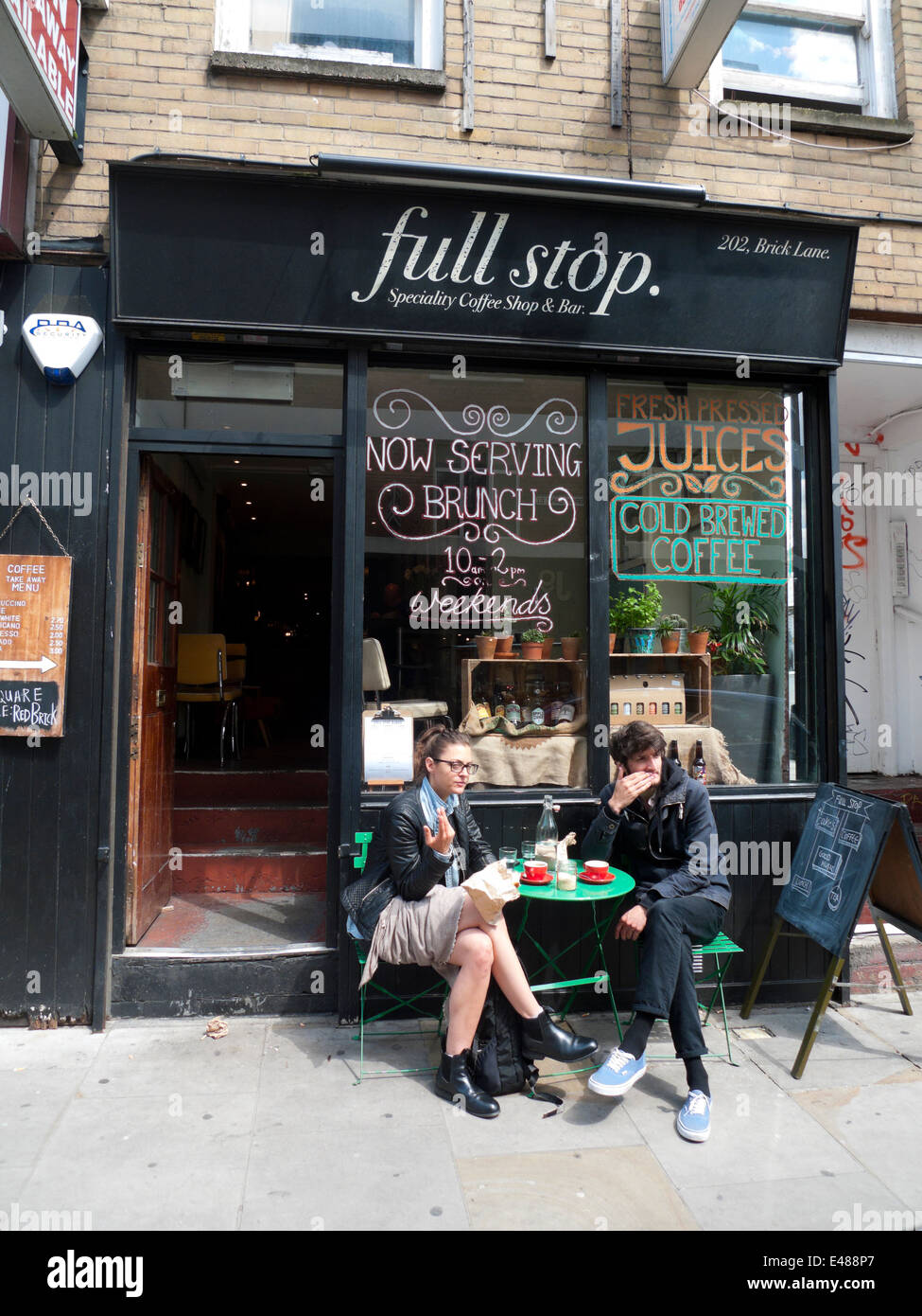 A young couple having a coffee at outside table Full Stop cate shop in Brick Lane Spitalfields East London E1 UK    KATHY DEWITT Stock Photo