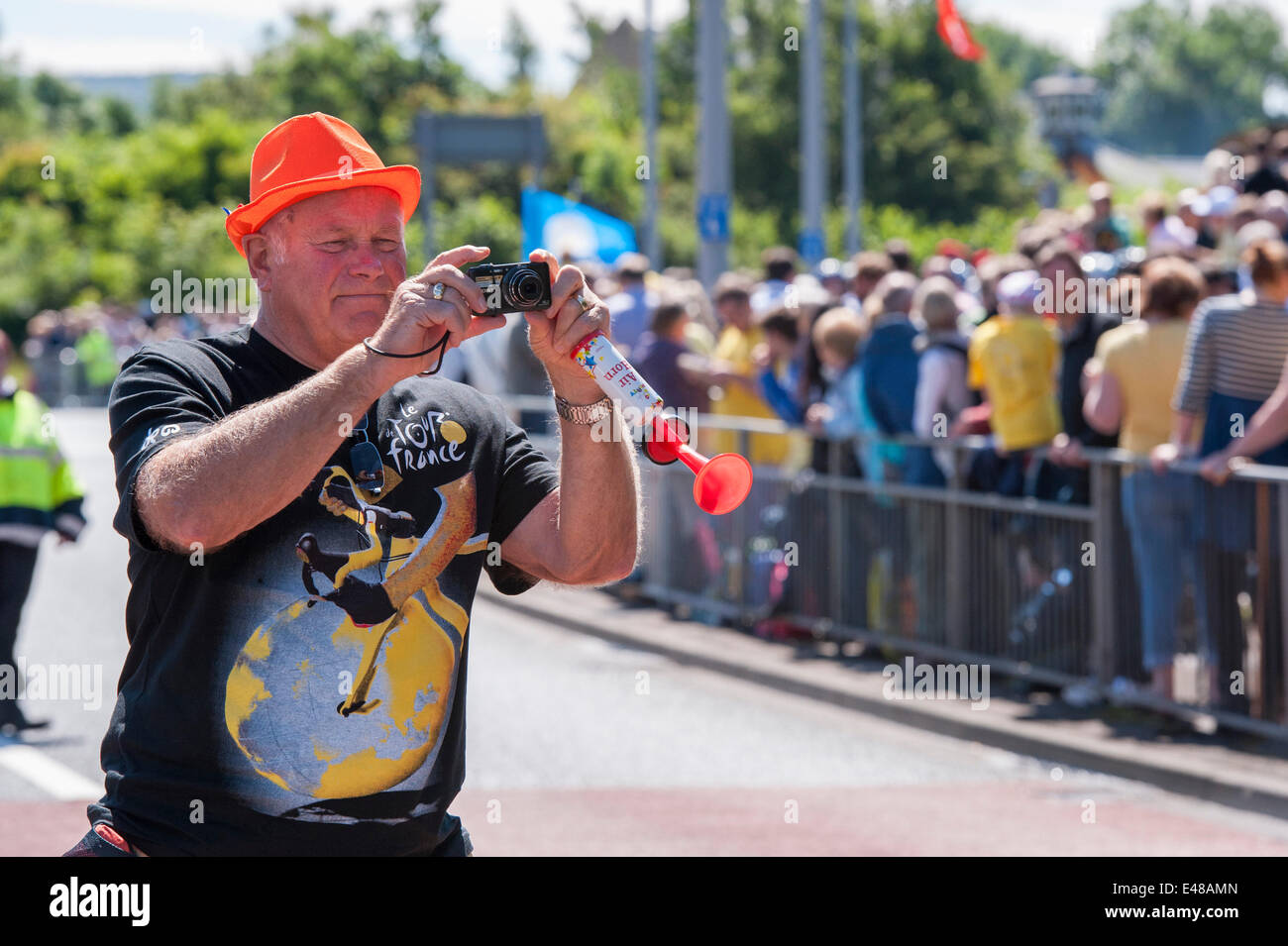 Burley-In-Wharfedale, Yorkshire, England, UK. July 5th 2014 .Large crowd of spectators stand behind barriers on the stage one route of the Tour De France, while 1 one man wearing an orange trilby sunhat, is leaning out, taking a photograph with a camera. Credit:  Ian Lamond/Alamy Live News Stock Photo