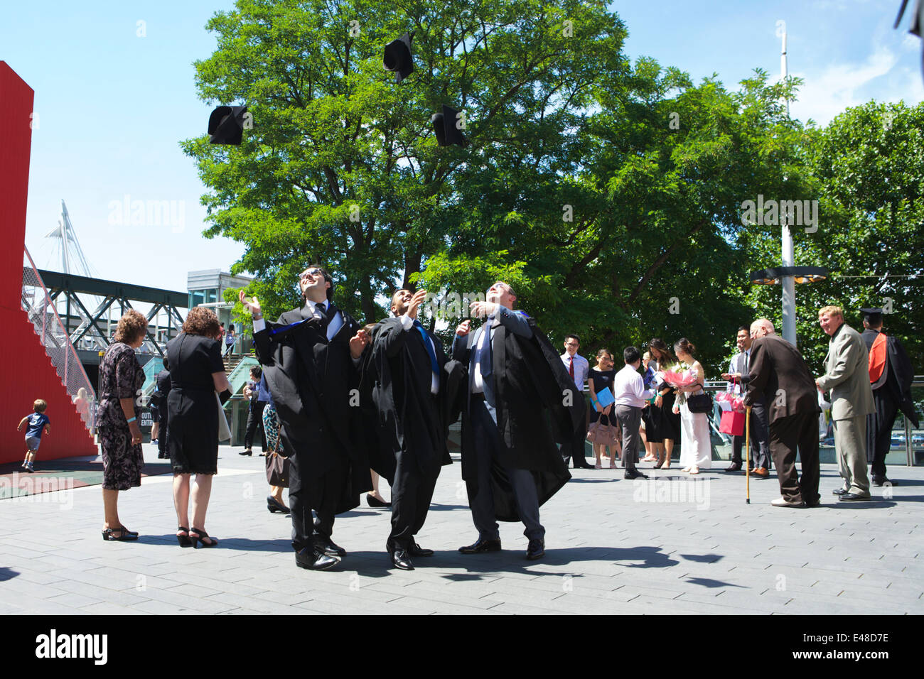 Graduation day: graduates wearing black gowns throw their caps in the air, Southbank, London, UK. Stock Photo