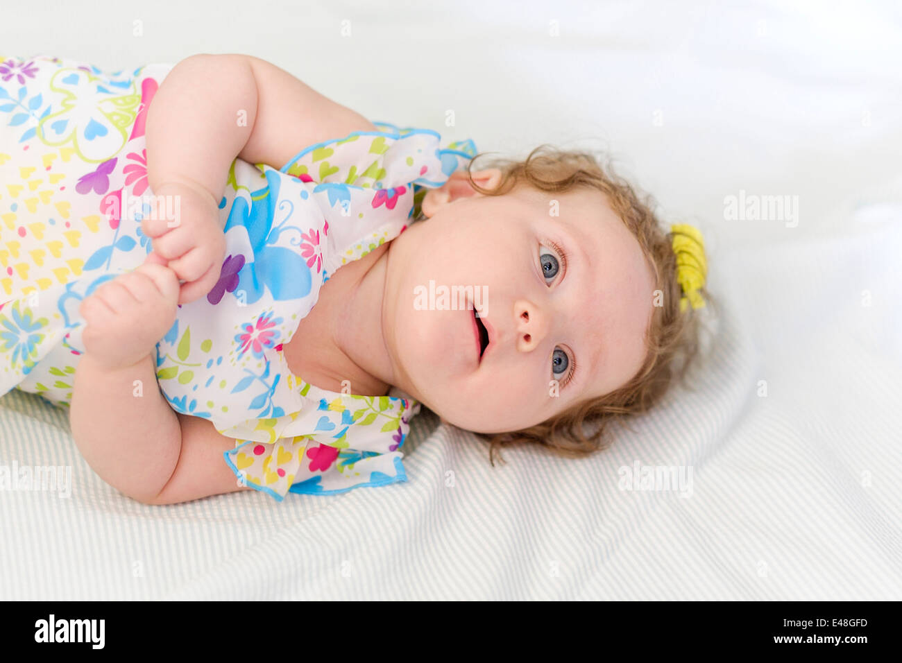 A beautiful three month old Caucasian infant girl lying on her back on a white blanket. USA. Stock Photo