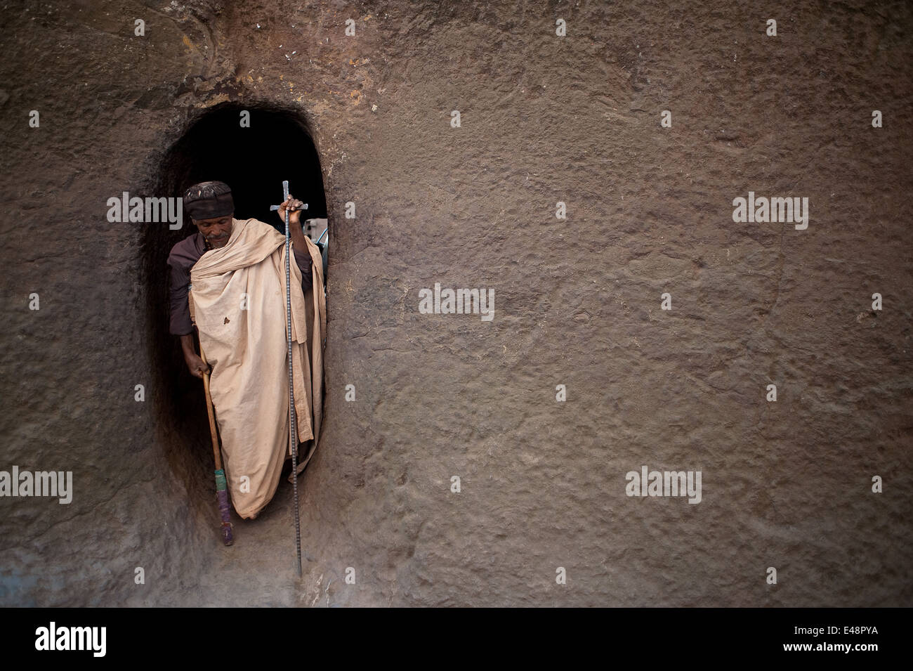 Orthodox man getting out of a tunnel connecting two rock hewn churches. The man is walking with a crutch ( Ethiopia) Stock Photo
