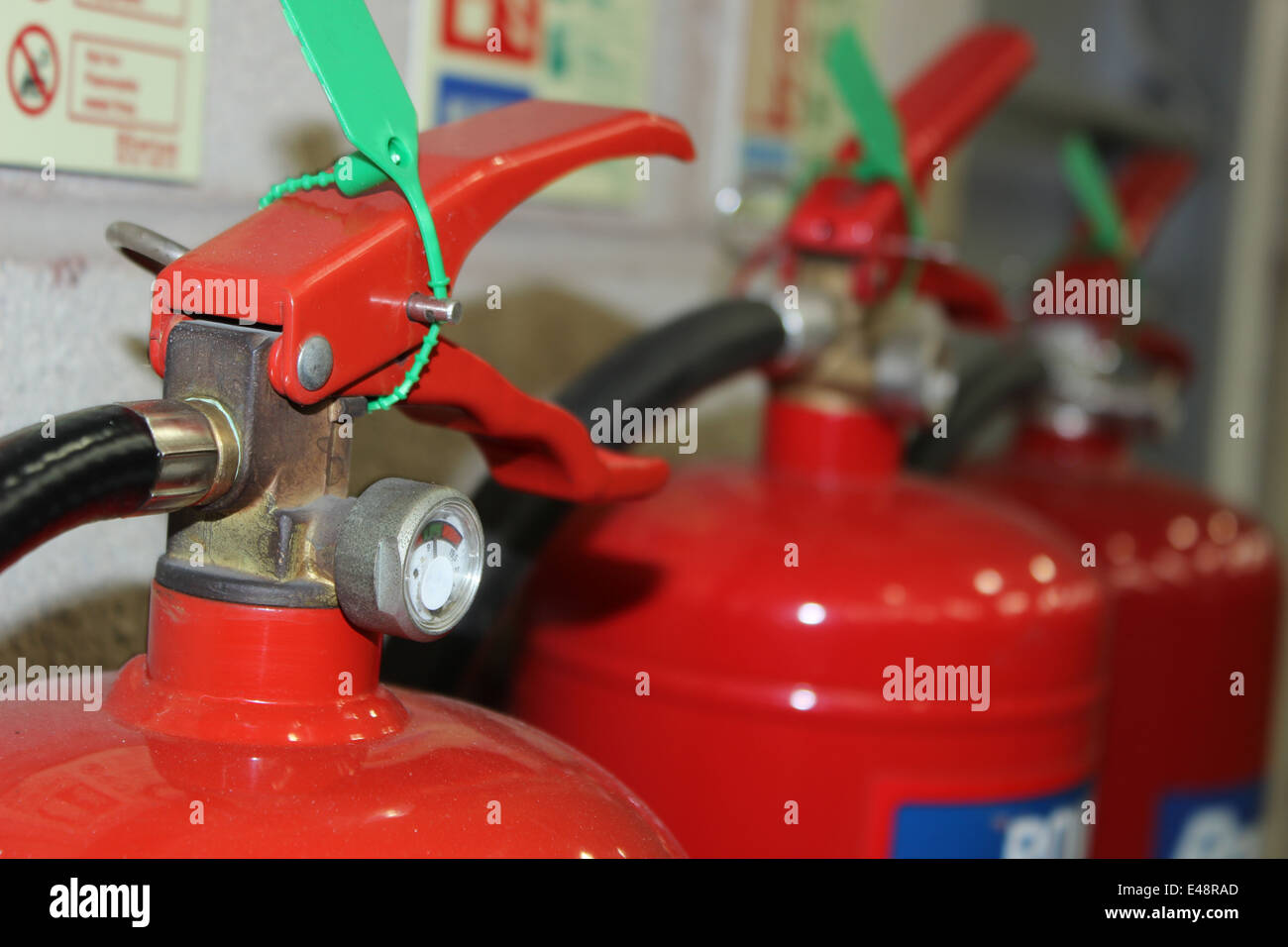 Close up of a red fire extinguisher on a warehouse wall with two other in the background. Stock Photo