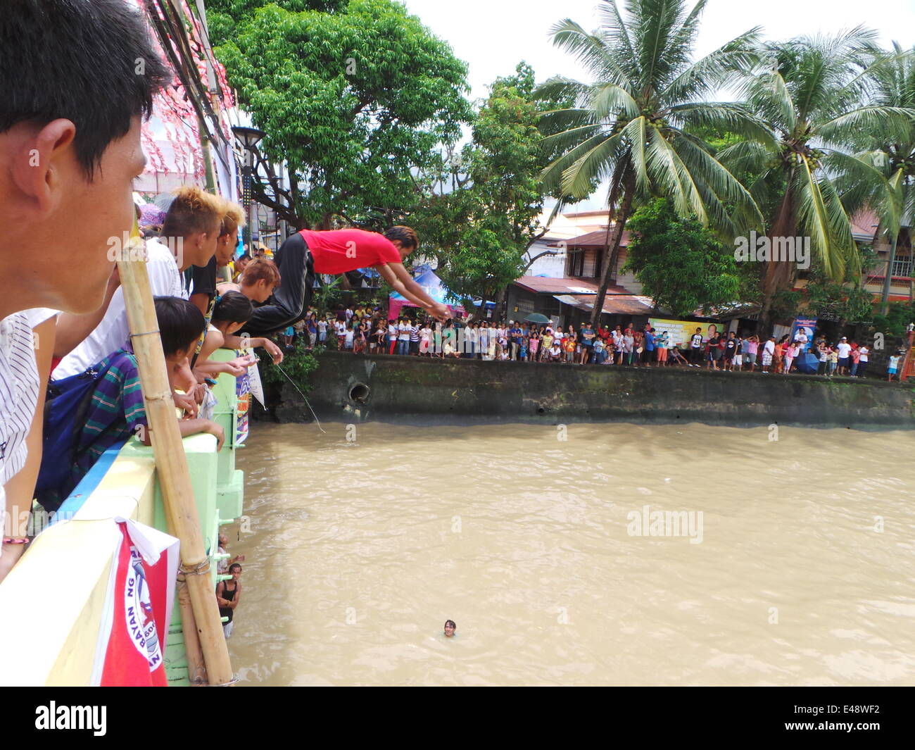 BOCAUE, BULACAN – JULY 6, 2014: Kids jumping at the bridge during the Pagoda sa Wawa which is held every first Sunday of July in Bocaue, Bulacan, in honor of the Holy Cross of the River (Mahal na Krus sa Wawa). The main attraction of the celebration is the fluvial parade of the pagoda or decorated barge and colorful small boats and people douching each other while on boats. Legend states that the forefathers of Bocaue extracted the Holy Cross from the river 200 years ago, and the celebration is in commemoration of this event. Twenty one years ago, in 1993, a tragic incident where 226 people dr Stock Photo