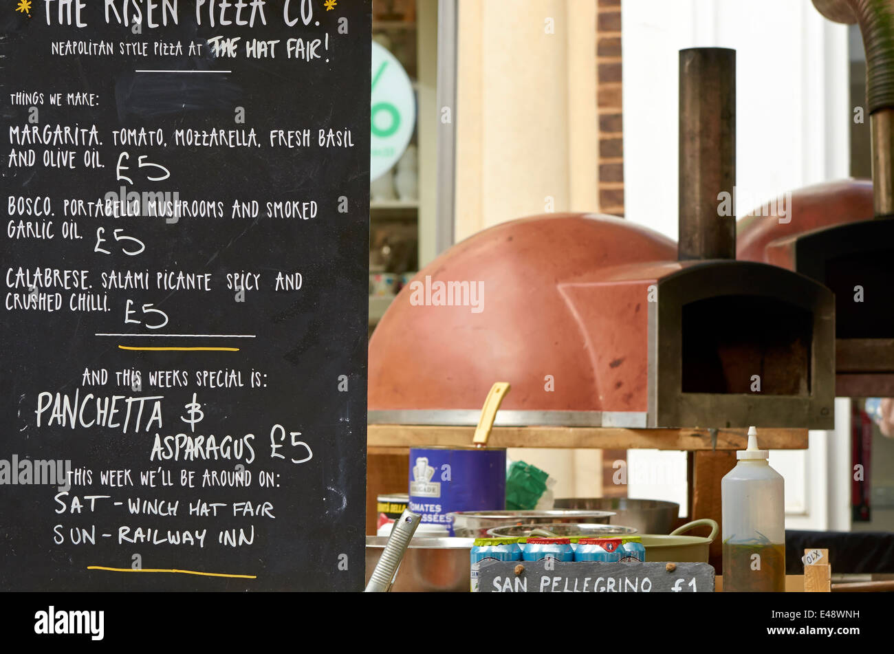 Menu board of a street market pizza stall with portable pizza ovens in the background. Stock Photo