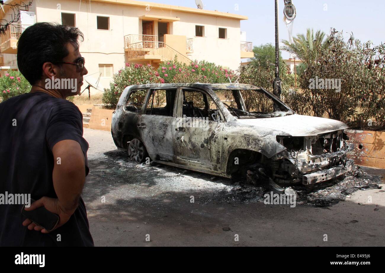 Tripoli, Libya. 6th July, 2014. A journalist looks at a damaged car in Janzour area of Tripoli, Libya, on July 6, 2014. Heavy fighting erupted in the Libyan capital city of Tripoli since the early hours of Sunday between the Interior Ministry's auxiliary security forces and a militia group called 'Knights Battalion', killing one person and injuring three others. (Xinhua/Hamza Turkia) Stock Photo