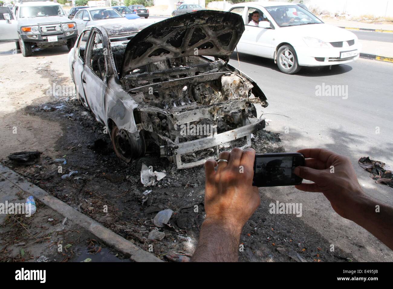 Tripoli, Libya. 6th July, 2014. A citizen takes a picture of a damaged car in Janzour area of Tripoli, Libya, on July 6, 2014. Heavy fighting erupted in the Libyan capital city of Tripoli since the early hours of Sunday between the Interior Ministry's auxiliary security forces and a militia group called 'Knights Battalion', killing one person and injuring three others. (Xinhua/Hamza Turkia) Stock Photo