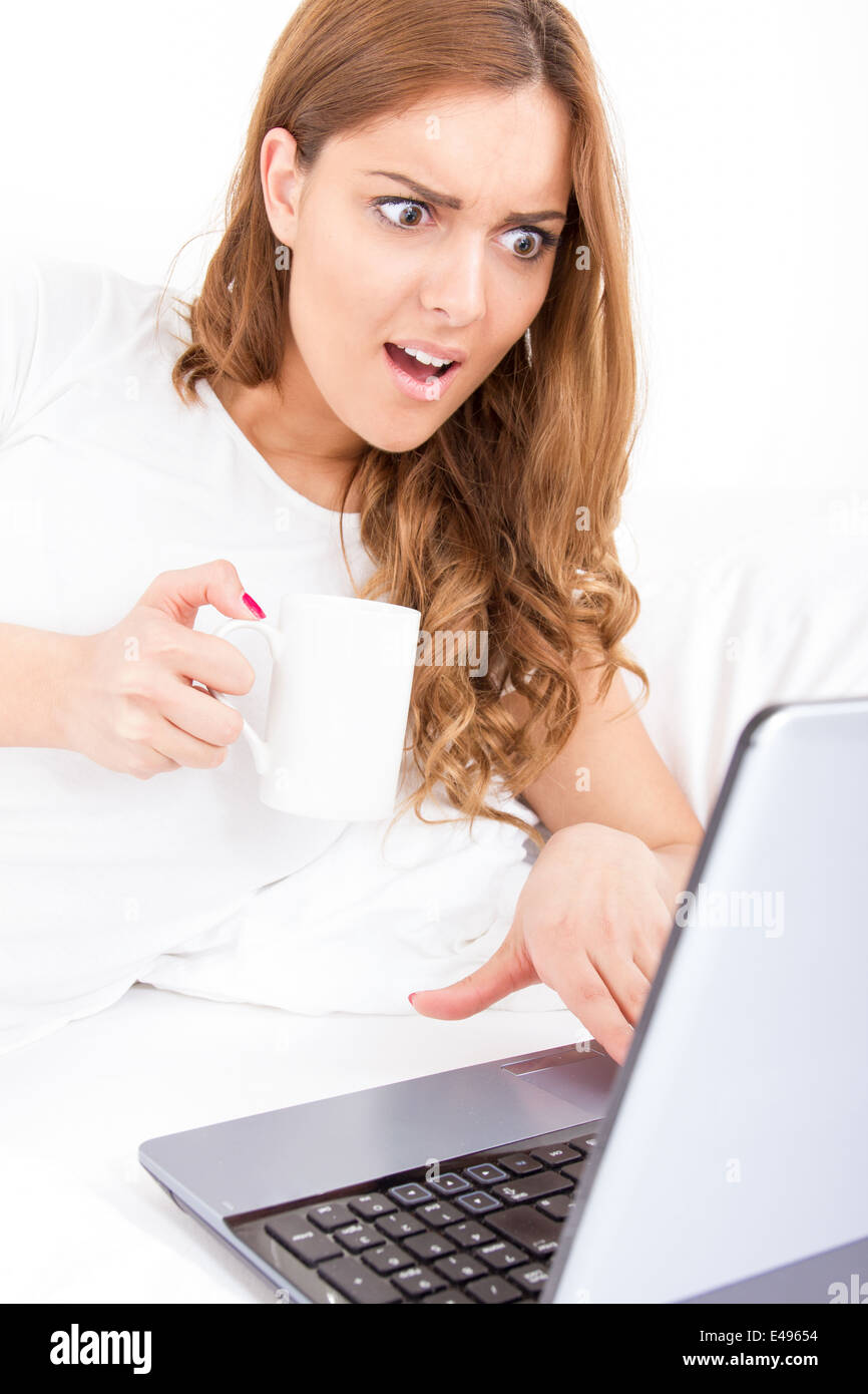 surprised worried woman looking in screen of laptop computer getting bad information while drinking coffee Stock Photo