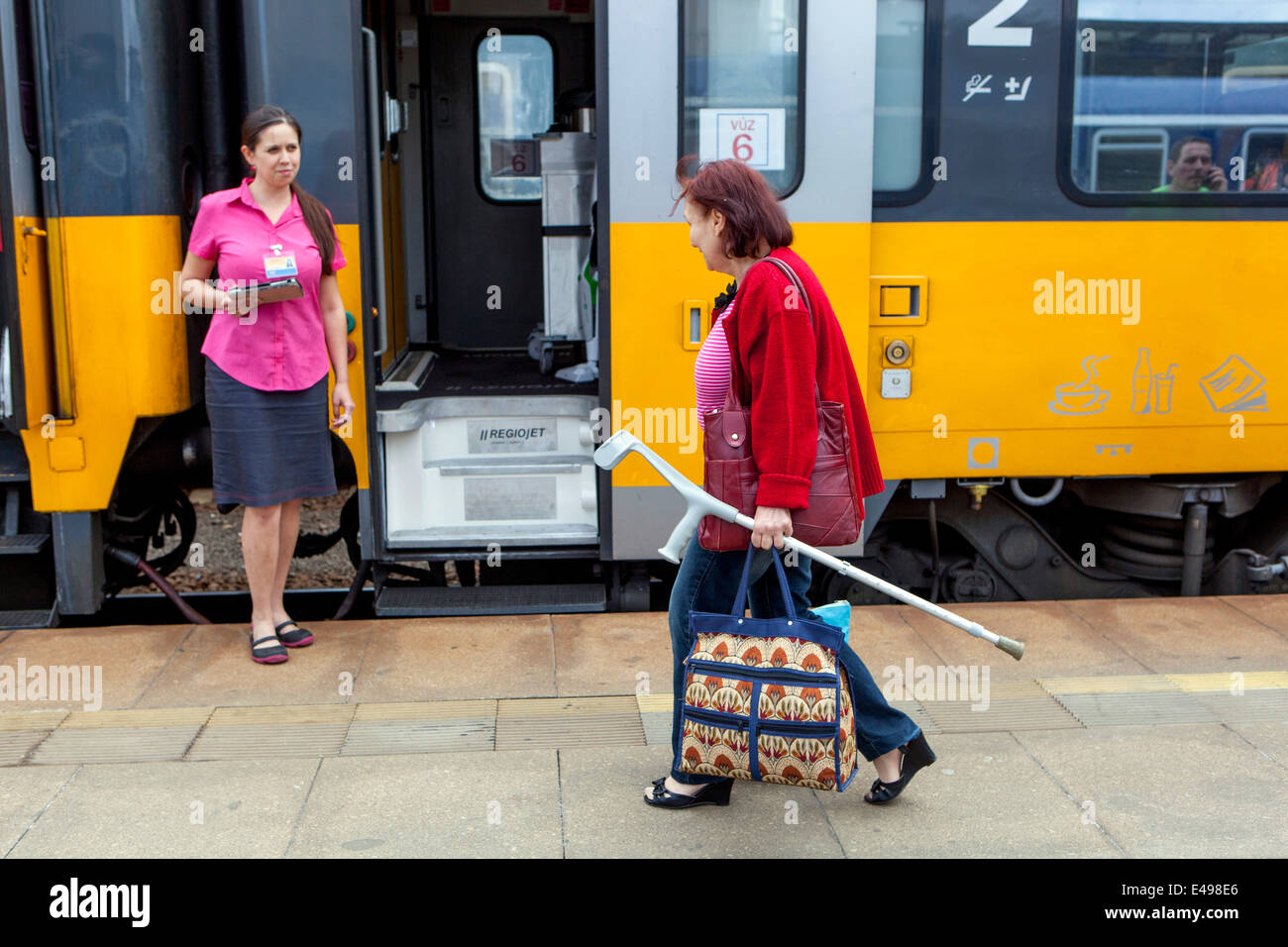 Senior woman passenger with crutch and conductor train at platform Prague, Czech Republic Stock Photo
