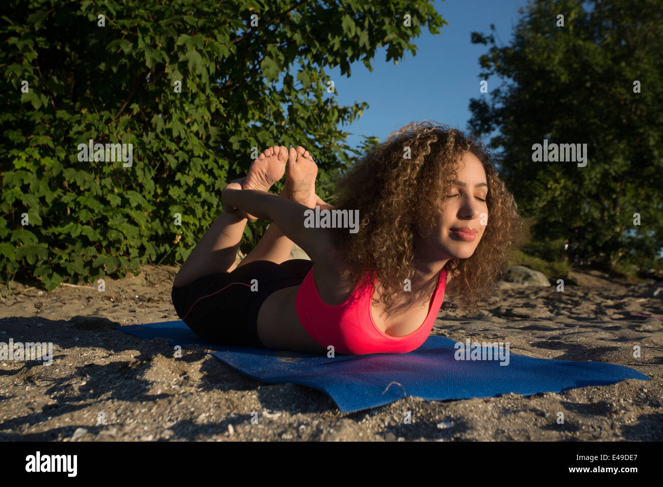 An attractive young woman does yoga on the beach with her eyes closed, smiling. Stock Photo