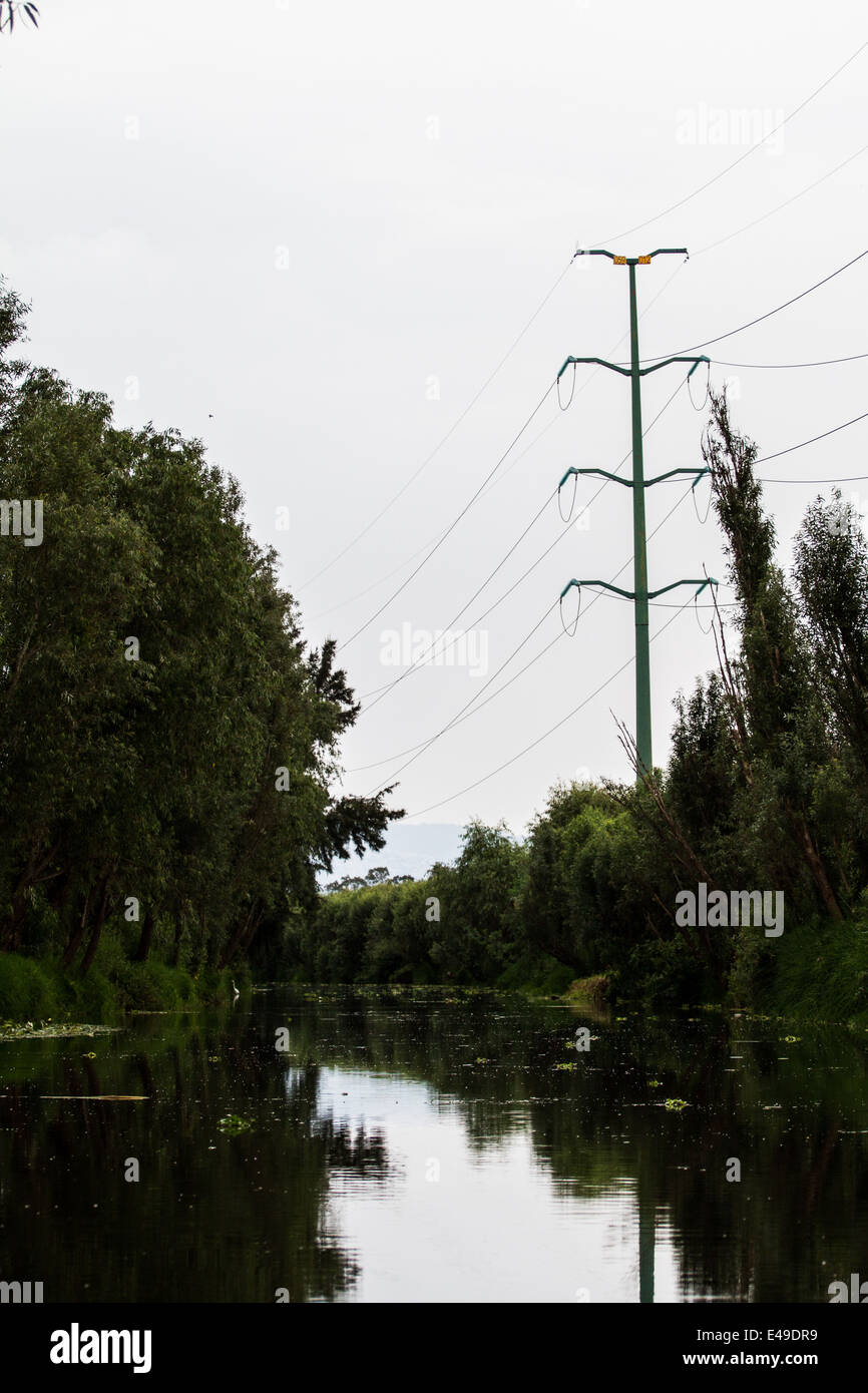Power lines high voltage tower by a river in a natural setup Stock Photo