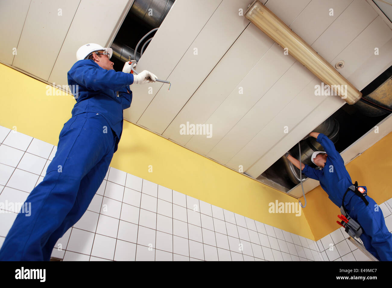 Two laborers working on ceiling piping Stock Photo