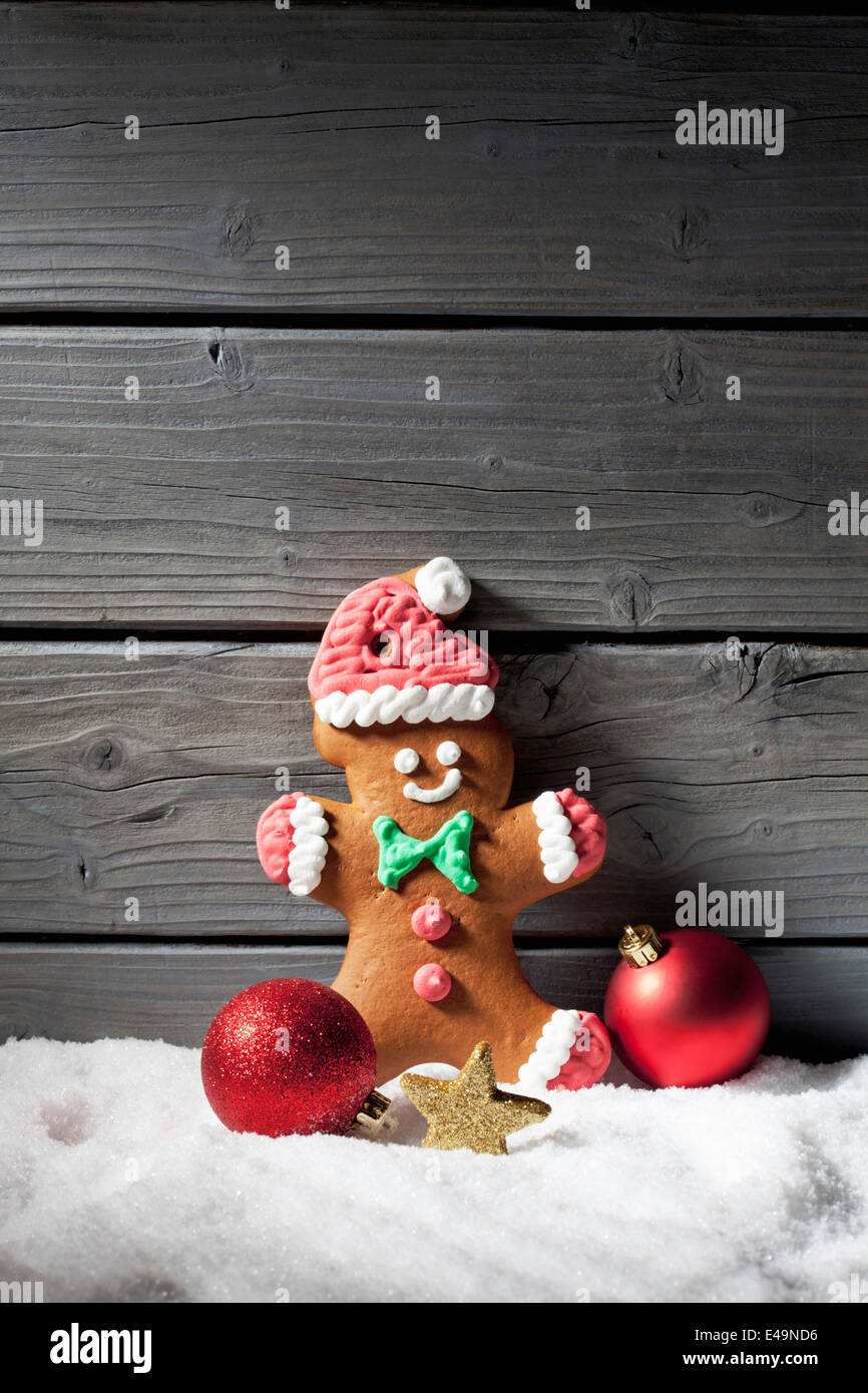 Gingerbread man and Christmas bubbles on artificial snow in front of grey wooden wall Stock Photo
