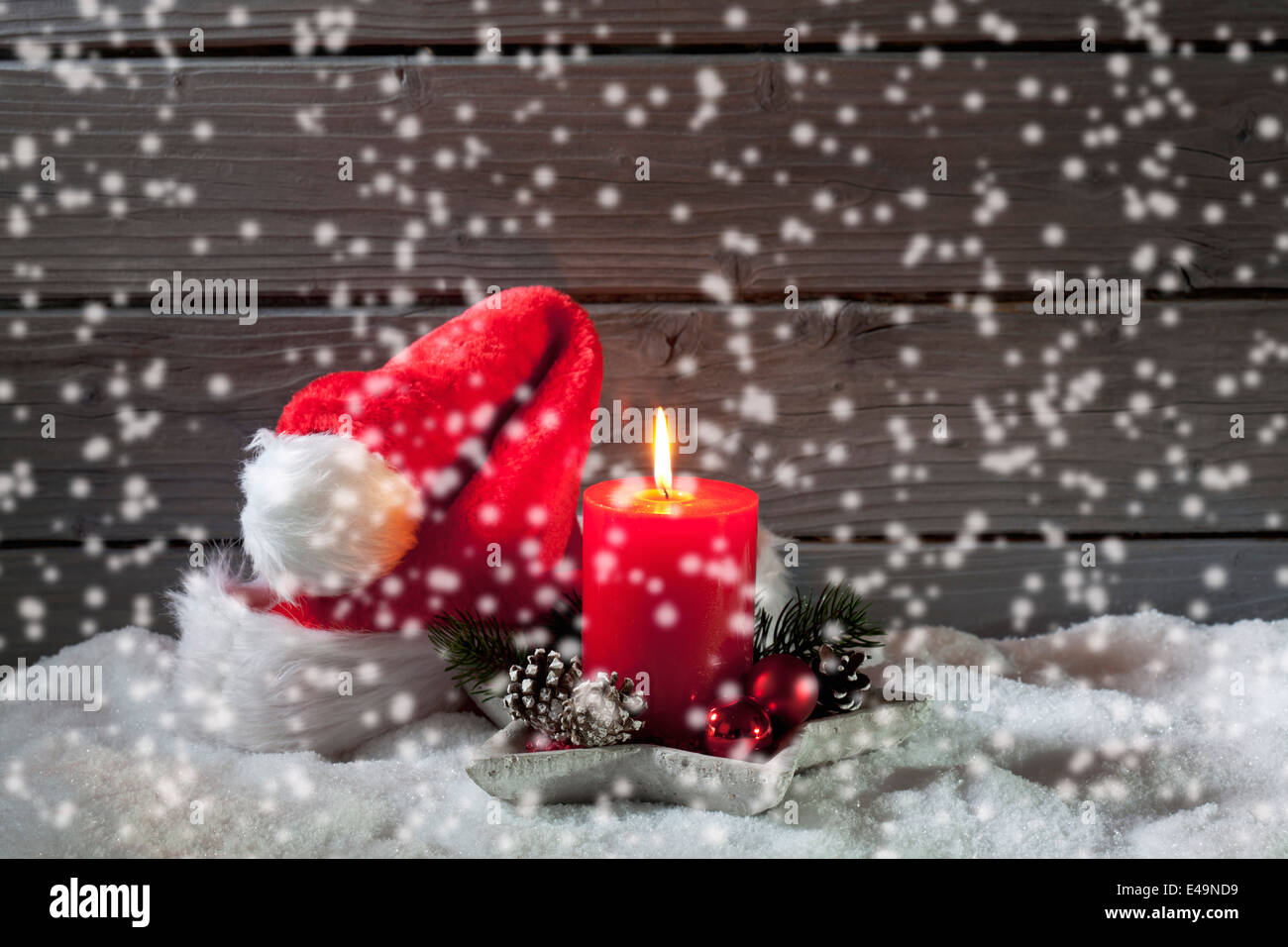 Lighted red candle and Christmas cap with rippling artificial snow in front Stock Photo
